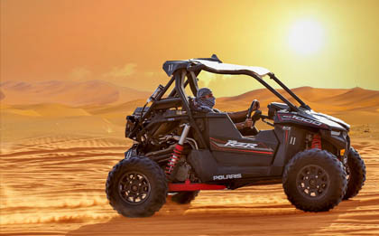 An adventurous solo desert safari experience in a one-seater dune buggy, racing across the golden sand dunes under the clear blue sky, creating a thrilling cloud of dust and sand behind.