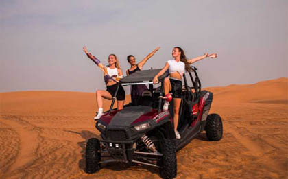 A four-seater desert safari buggy roaring through the endless expanse of desert dunes, with all four passengers securely strapped in, navigating the rugged terrain, and leaving a trail of sand and excitement in their wake.