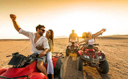 A thrilling morning desert safari adventure with quad bikes. The rising sun bathes the sandy desert landscape in a soft, golden light as riders on powerful quad bikes traverse the dunes, leaving a trail of excitement and adrenaline in their wake under the clear morning sky.